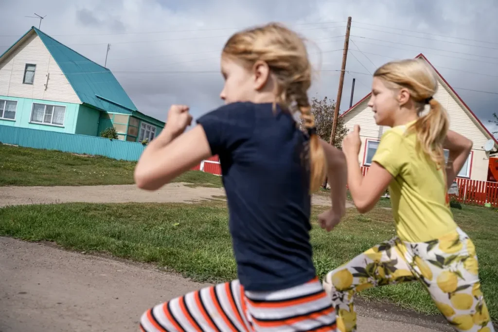 Даша и Полина Фельхле бегут по селу Корнилово в 150 км от Новосибирска. Их папа Юрий работал слесарем, потом перешел в местный сельский свинокомплекс, который в 2022 году закрыли из-за долгов. Чтобы содержать семью, Юрий берется за любую подработку. Его семье помог центр поддержки семей и детей «Вместе». Фото: Дмитрий Яцюк.