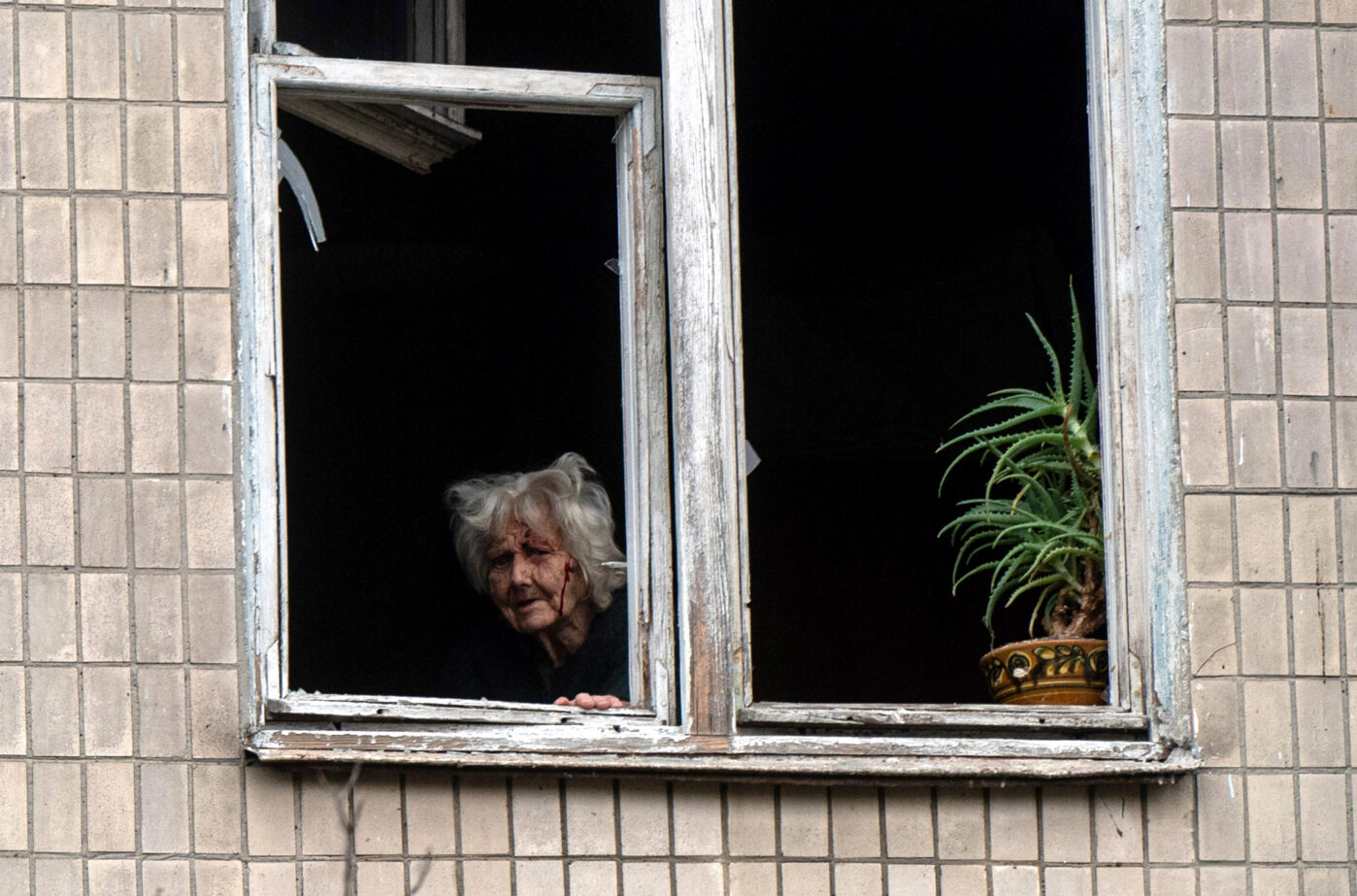 Раненая пожилая женщина смотрит в&nbsp;разбитое окно пятиэтажного жилого дома, поврежденного российским беспилотником в&nbsp;Святошинском районе Киева
